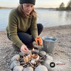 Kvinna tänder en tändsticka vid en stenring på en grusstrand med den orange behållaren i andra handen och en hink vatten bredvid