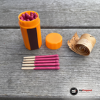 Orange behållare, lock och fem tändstickor med rosa huvuden bredvid en rulle björknäver på ett grått träbord