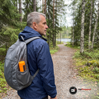 Vandrare med grå ryggsäck på en skogsväg, den orange behållaren med tändstickor sticker upp ur fickan på ryggsäckens sida