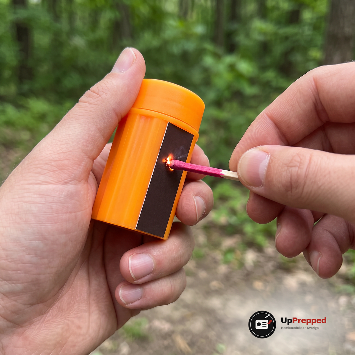 Tändsticka med rosa huvud dras mot den mörkbruna tändytan på den orange behållaren, nära bild