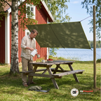 Olivgrön tarp uppspänd som solskydd över ett picknickbord framför en röd stuga vid en sjö, medan en man häller upp kaffe