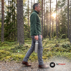 Man går på en grusstig i tallskog med en titanflaska hängande i bäröglan i handen