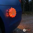 Orange varningsljus fäst med magnet på ett blått bilskärm i skymningen med röd-orange ljus