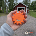 Hand som håller ett orange magnetiskt LED varningsljus framför ett rött garage med grusuppfart