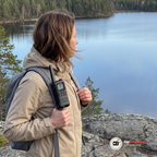 Kvinna med ryggsäck vid en sjö med en walkie talkie fäst på axelremmen
