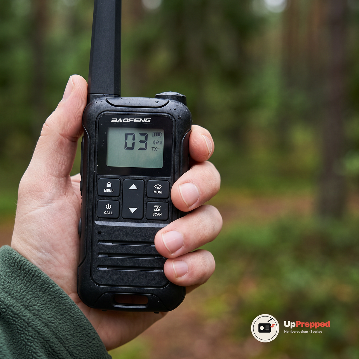 Närbild på en walkie talkies display och knappar i en hand framför en suddig skog