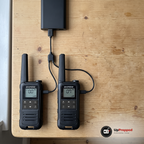 Två walkie talkies som laddas från en powerbank med en 2-i-1-kabel på ett träbord